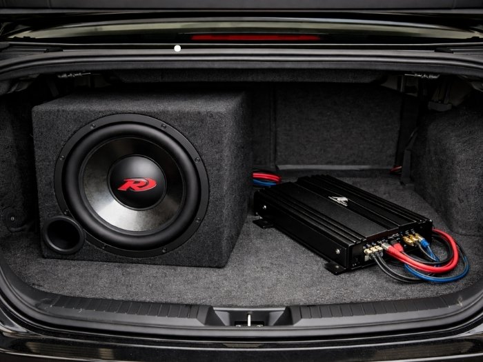 A professional car audio setup inside a vehicle trunk featuring a custom subwoofer enclosure box, an amplifier, and clean wiring.