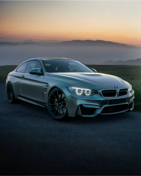 A sleek silver luxury coupe showcasing high-performance window tint parked against a misty horizon during a picturesque sunset.
